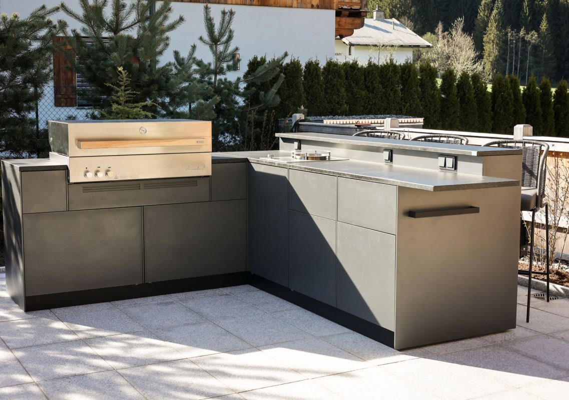 Graue Outdoorküche in L-Form mit Edelstahlgrill auf einer Dachterrasse in Kitzbühel mit Bergblick