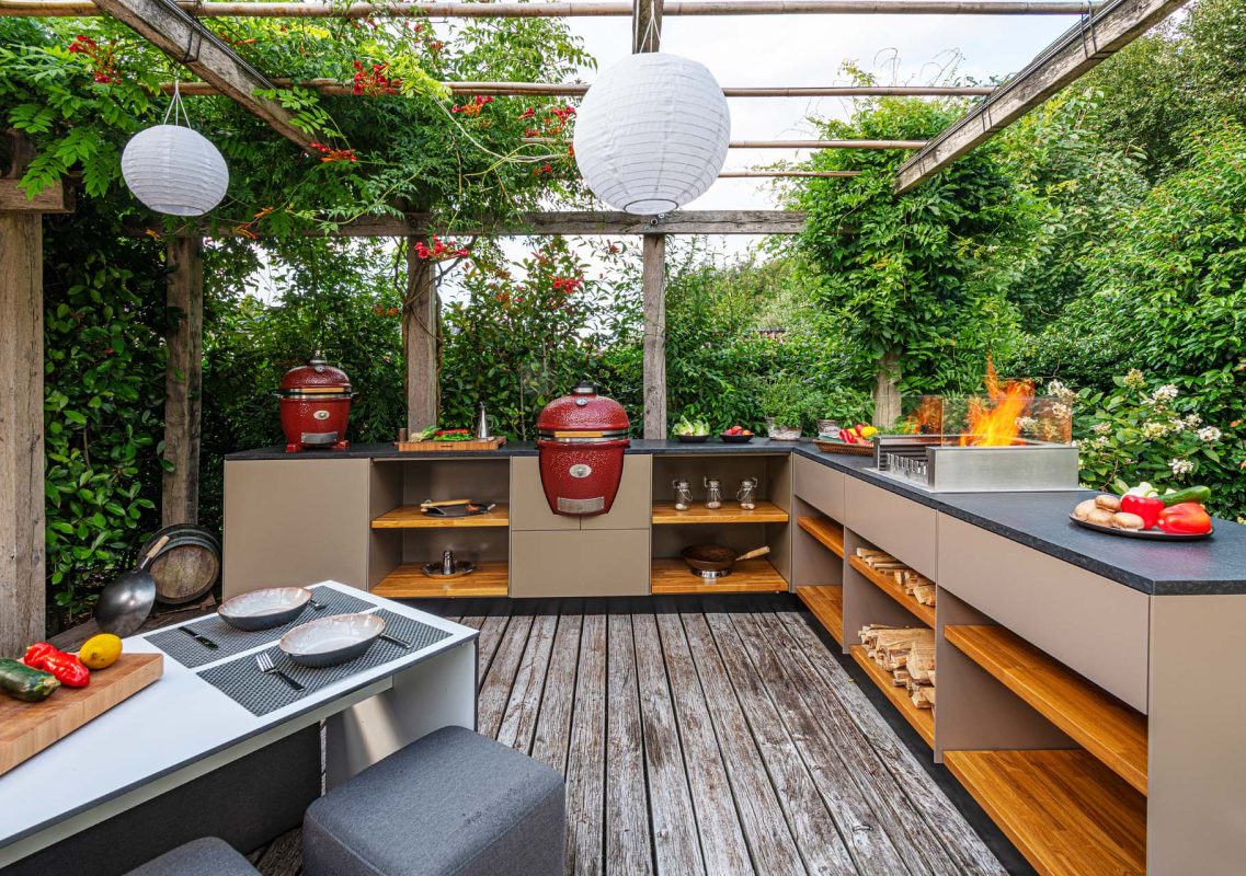 Beige Outdoorküche mit roten Kamados unter einer berankten Pergola