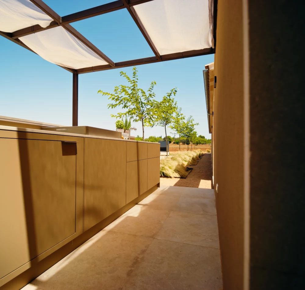 Sandfarbene Outdoorküche unter einer Pergola auf Mallorca, entlang der Hauswand geplant