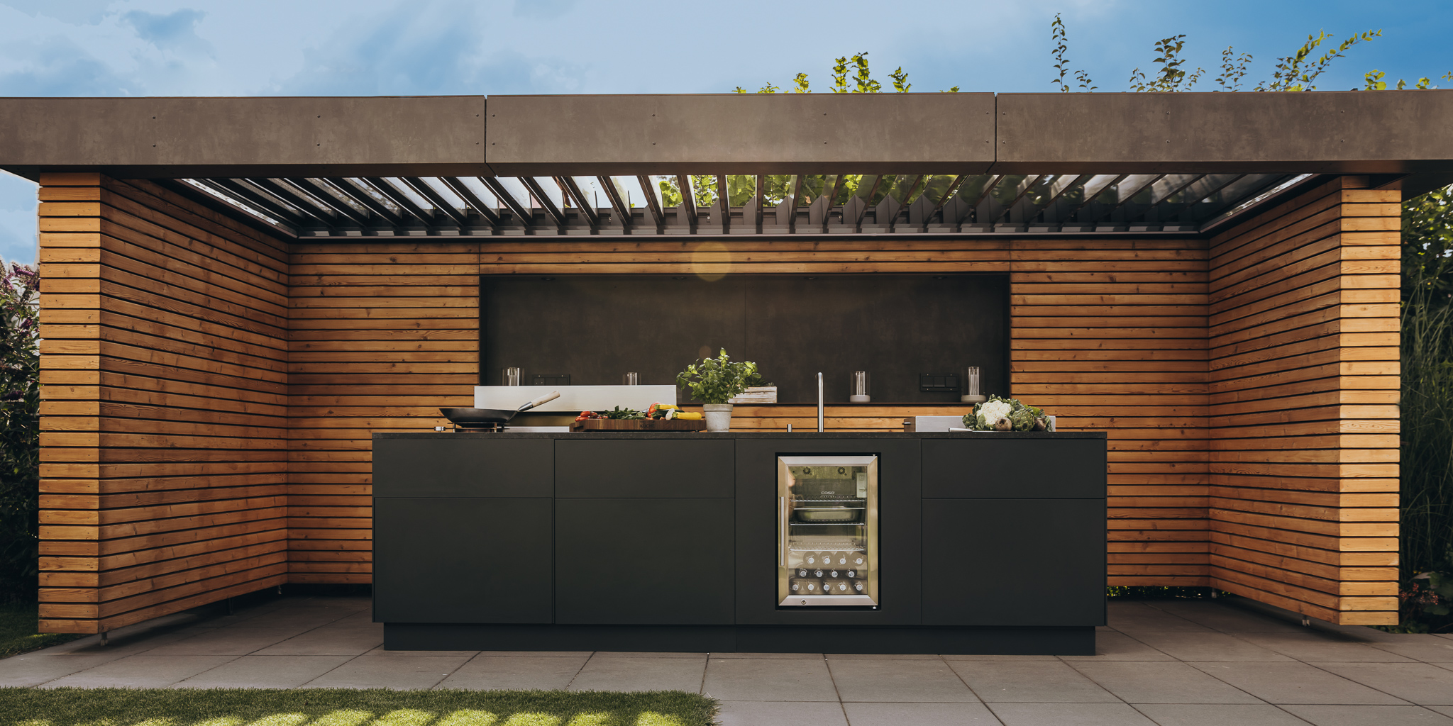 Outdoor-Küche mit verschiedenen Elementen wie Kühlschrank und Grill in einem einladenden Ambiente.