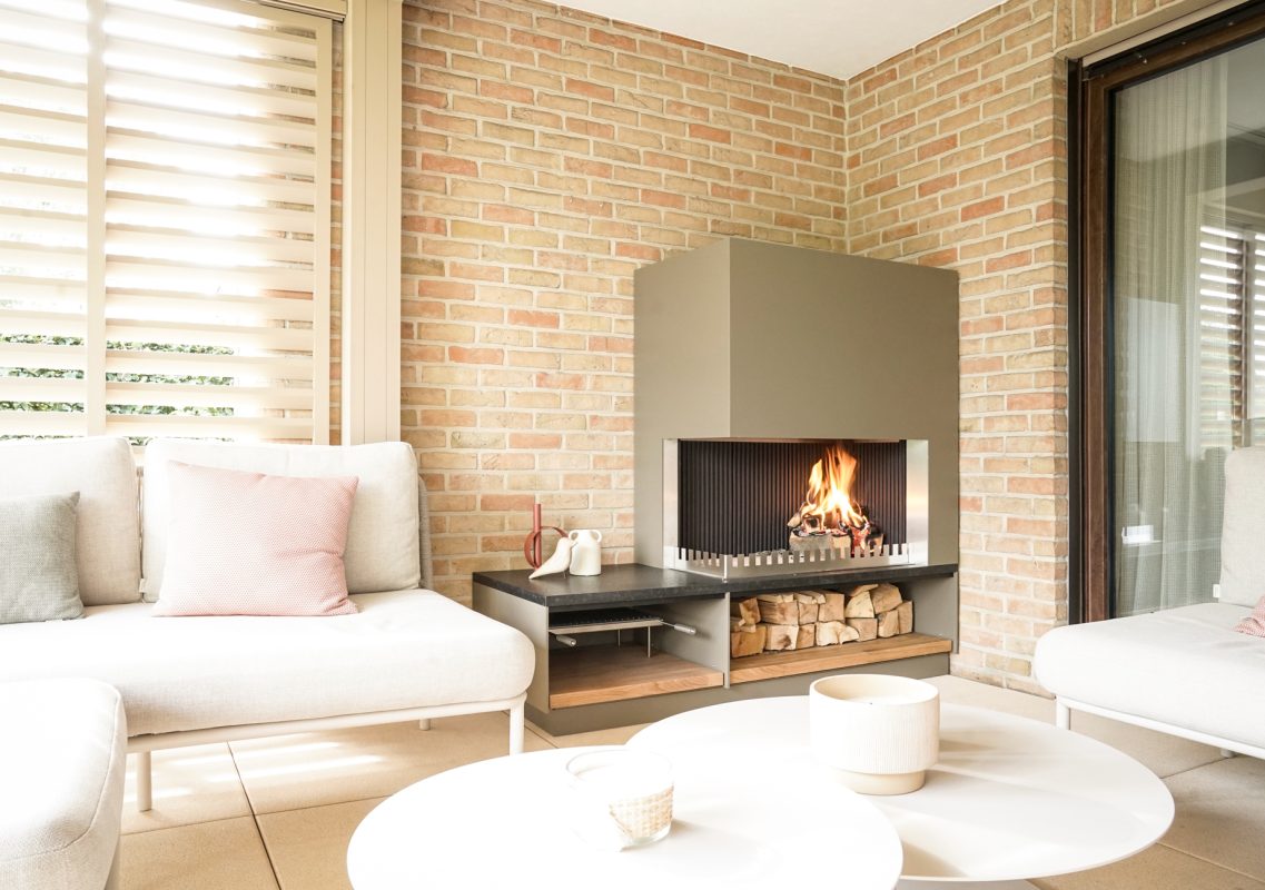Helle Lounge mit Kamin und Holzlager hinter dem runden Couchtisch
