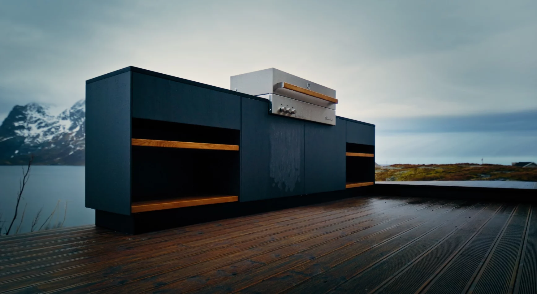 Dunkelblaue Kücheninsel mit Grill auf einer Holzterrasse am Fjord in Norwegen