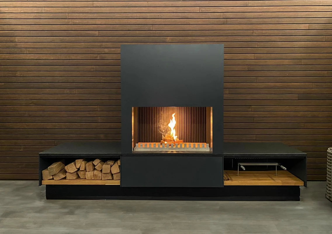 FREILUFT Feuer mit Grill-Feuerstelle mit Holzlager vor dunkler Holzwand
