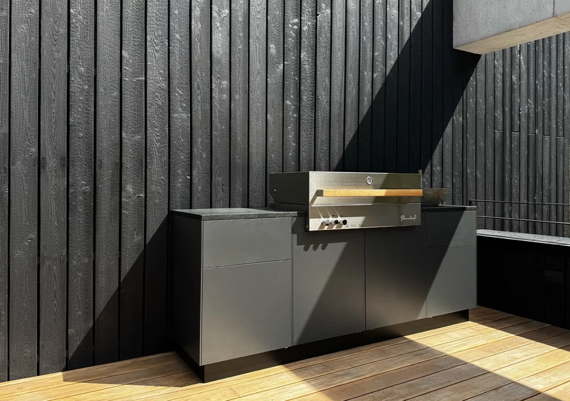 Graues Küchenmodul mit Gasgrill vor schwarzer Holzfassade